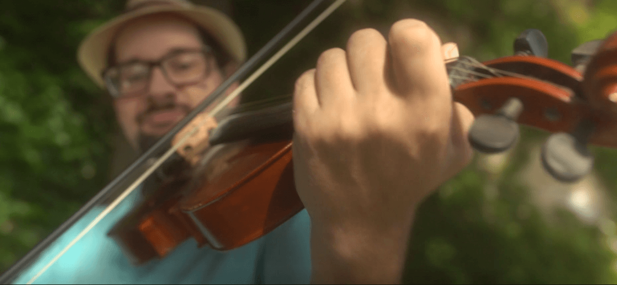 A man wearing a hat is playing a violin.