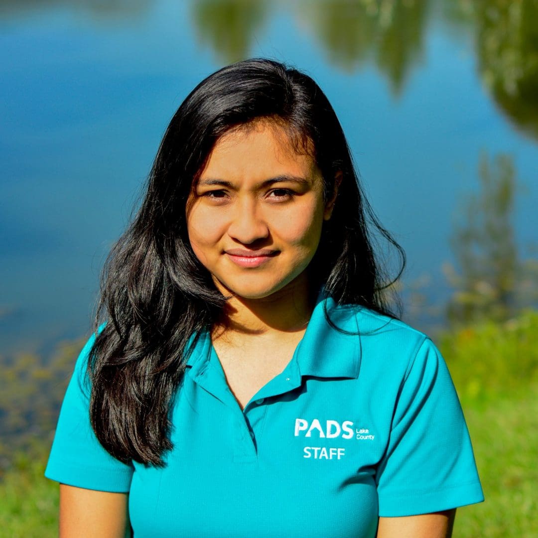 A young woman in a blue polo standing in front of a lake.