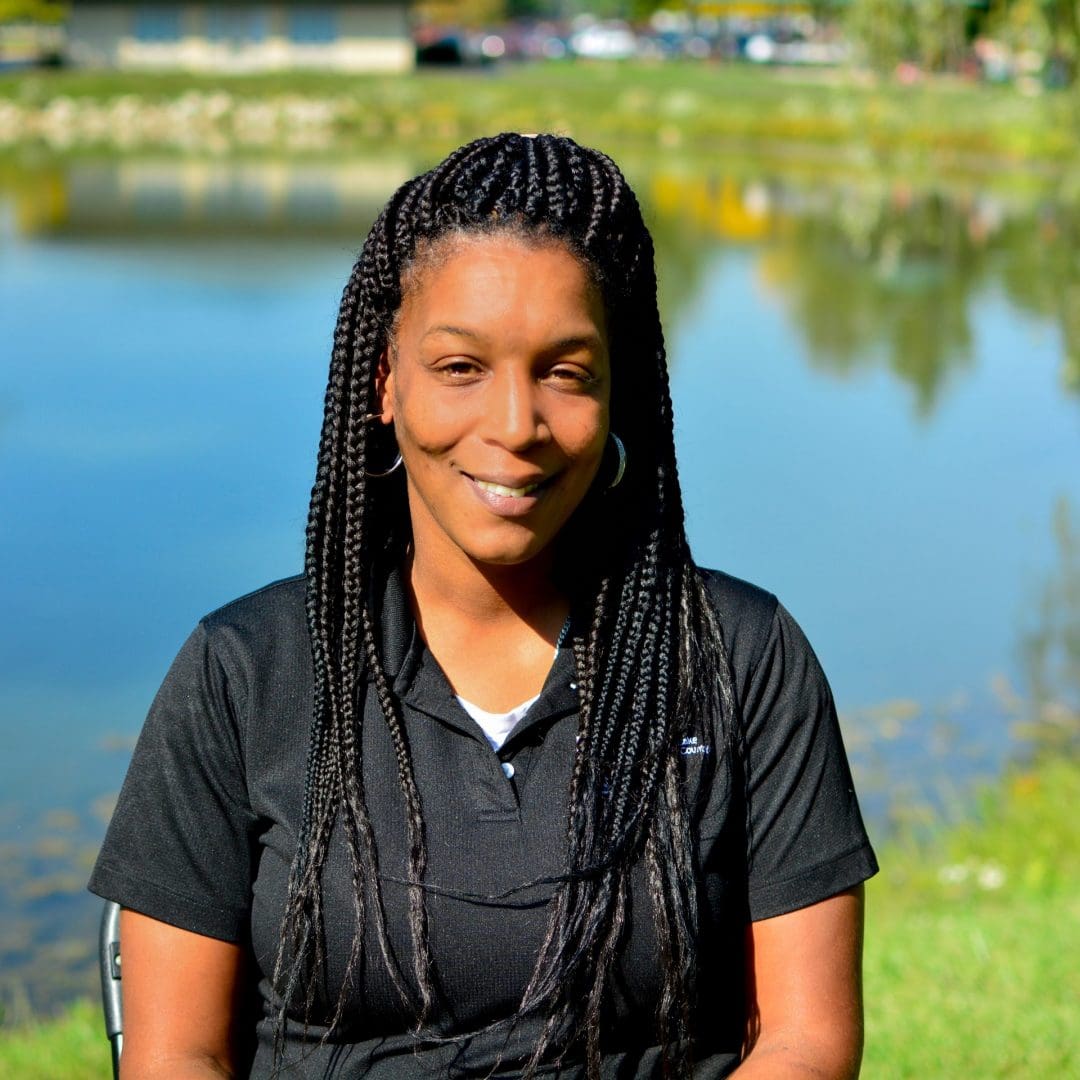 A black woman sitting in front of a pond.